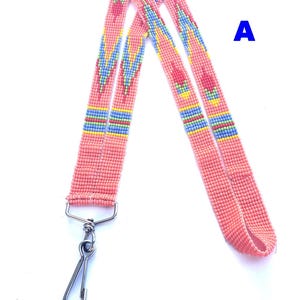 May include: A pink beaded lanyard with a silver metal clasp. The lanyard has a repeating pattern of blue, yellow, and red beads. The letter "A" is in blue in the upper right corner.