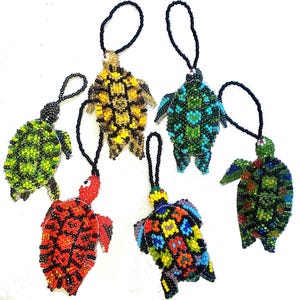 May include: A collection of six beaded turtle ornaments in various colors, including green, yellow, red, and blue. Each turtle has a black beaded loop for hanging. The turtles are intricately detailed with beadwork.