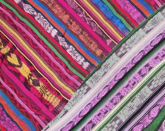 Puede incluir: Una tela textil que presenta un vibrante patrón diagonal de rayas multicolores. El diseño incluye bandas alternas de rosa brillante, amarillo, azul, verde y naranja, intercaladas con intrincadas texturas tejidas y motivos repetitivos.