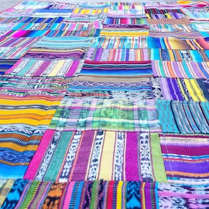 May include: A colorful patchwork quilt with a variety of vibrant fabric patterns. The quilt features a mix of stripes, geometric designs, and solid colors in shades of blue, pink, yellow, and purple. The quilt is made of multiple rectangular pieces.