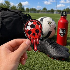 May include: A red and black soccer skull sticker is held in front of a soccer ball, cleats, and a red water bottle. The sticker has a soccer ball design with a skull shape and dripping blood effect. The water bottle has the text "PITCH PLEASE".