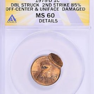 May include: A copper 1975-D 1C MS 60 coin, double struck and 85% off-center, encased in a clear holder. The coin's details are visible, with the text "1975-D 1C" and "DETAILS" printed on the holder. The coin is damaged.