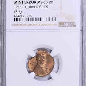 May include: A 1957 D 1C penny coin, graded MS 63 RB, with a mint error of triple curved clips, encased in a protective holder. The coin weighs 2.7g and is certified by Numismatic Guaranty Corporation.