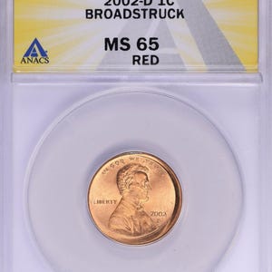 May include: A 2002-D 1C MS 65 red penny coin in a protective case. The coin features the text "IN GOD WE TRUST" and "LIBERTY". The case also displays "2002-D 1C BROADSTRUCK MS 65 RED".