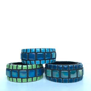 May include: Three ceramic rings with a mosaic design. The rings are stacked on top of each other. The top ring is blue, the middle ring is green, and the bottom ring is blue.
