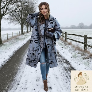 Może przedstawiać: Szary płaszcz z czarnym wzorem twarzy jest noszony w zaśnieżonej scenerii na zewnątrz. Płaszcz sięga do kolan i ma powtarzający się wzór stylizowanych twarzy. Osoba nosi niebieskie dżinsy i brązowe buty.