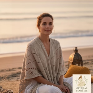Peut inclure: Une femme porte un châle beige en tricot ajouré avec un col en V. Le châle présente un motif géométrique et est drapé sur des vêtements blancs. L'image est prise sur une plage au coucher du soleil, avec le logo "Mistral Bohème".