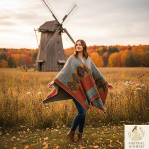 Peut inclure: Une personne porte un poncho à motifs avec des motifs géométriques rouille, sarcelle et or. Le poncho est drapé sur les épaules. En arrière-plan, un moulin à vent, un champ d'herbes hautes et des arbres aux couleurs d'automne.