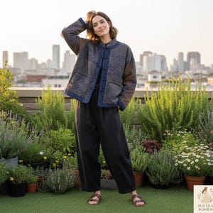 Peut inclure: Veste matelassée à col mandarin dans les tons de bleu, marron et gris. La veste présente un motif floral et est associée à un pantalon noir et des sandales marron. L'arrière-plan présente un jardin sur le toit et une ligne d'horizon urbaine.