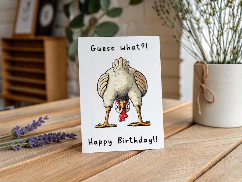 May include: A white greeting card with a cartoon chicken illustration. The chicken is upside down, with its rear end facing the viewer. The text "Guess what?!" and "Happy Birthday!!" are printed on the card.