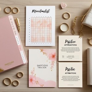 Può includere: Una composizione piatta di articoli di cancelleria tra cui un'agenda rosa e oro, quaderni, penne e anelli. L'agenda ha una rilegatura a spirale dorata. Ci sono anche carte con il testo "Positive Affirmations", "Emotions Tracker" e "Mini Habit List".