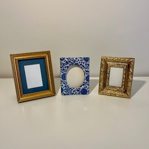 May include: Three picture frames arranged in a row. The left frame is gold with a dark blue mat and a rectangular opening. The center frame is rectangular with a blue and white floral pattern and an oval opening. The right frame is gold with a textured border and a rectangular opening.