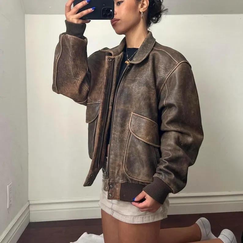 Close-up of vintage leather bomber jacket showing soft aged brown texture, handmade stitching details, and durable zipper front — classic grunge retro outerwear.