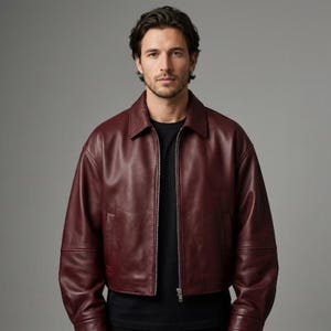 May include: A deep burgundy leather jacket featuring a classic collar, long sleeves with cuffs, and a central metal zipper closure. The jacket is worn over a plain black shirt, showcasing a smooth finish and a structured, waist-length silhouette.