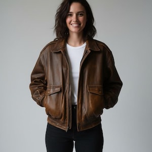 May include: A brown leather bomber jacket featuring a collared neckline, a front zipper closure, and two large flap pockets on the front. The jacket has an elasticized waistband and cuffs, with a distressed finish throughout the leather material.