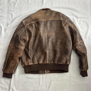 Model wearing vintage brown leather bomber jacket in oversized style, ribbed cuffs and waist, classic aviator retro look perfect for everyday wear.