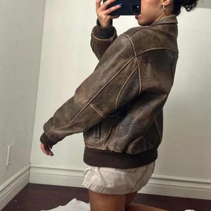 Unisex 90s vintage oversized leather jacket styled with casual outfit, featuring front flap pockets and relaxed fit for both men and women.