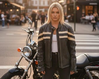 Op de afbeelding: Een zwart leren motorjack met twee horizontale crèmekleurige strepen over de borst en mouwen, een opstaande kraag met drukknoop en ritsen bij de mouwen, gedragen over een effen wit shirt en een donkere spijkerbroek.