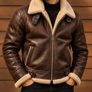 Op de afbeelding: Een donkerbruine leren jas met een dikke beige shearling kraag en voering. De jas is voorzien van een ritssluiting over de gehele lengte, twee zijzakken, verstelbare gespriemen bij de kraag en taille, en shearling boorden aan de mouwen.