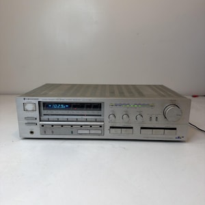 Puede incluir: Un receptor estéreo de alta velocidad computarizado Kenwood KR-930 plateado con una pantalla digital que muestra 102.9, múltiples perillas de control, botones, un conector para auriculares y una serie de luces indicadoras verdes en el panel frontal.