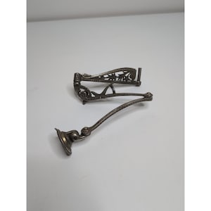 May include: Two antique silver-toned metal objects. One is a decorative, hinged piece with floral cutouts. The other is a curved arm with a circular base. Both pieces appear to be components of a larger item.