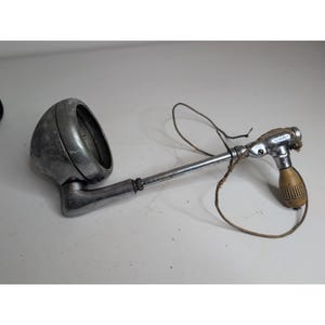 May include: A vintage chrome-plated spotlight with a rounded housing and a long, adjustable metal arm. The assembly features a small, light-coloured wooden handle at the end of the arm and a thin, frayed brown string looped around the metal components.