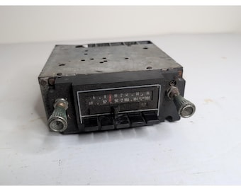 May include: Vintage car radio with a silver metal casing and a black faceplate. The faceplate features a frequency dial and buttons. Knobs are on either side. The radio displays frequencies from 88 to 108.