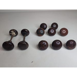 May include: A collection of ten round, dark brown, mottled ceramic door knobs. Two knobs are attached to metal spindles, while the remaining eight are individual knobs. The surfaces feature a glossy, marbled finish with varying dark brown tones.
