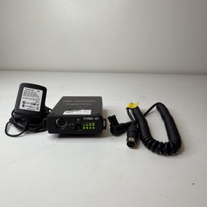 May include: A black Quantum Turbo SC battery charger with a power adapter and coiled cable. The charger has a series of green indicator lights and the text "TURBO SC". The power adapter is labeled "QUANTUM T86".