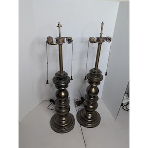 Puede incluir: Dos lámparas de mesa vintage de latón. Cada lámpara tiene un diseño de bolas apiladas en la base y un cuello largo y esbelto. Las lámparas tienen cadenas y están cableadas para electricidad. Las lámparas miden aproximadamente 76 cm de alto.