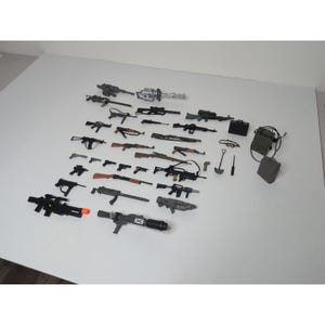 以下が含まれることがあります： さまざまなサイズと色の、ライフル、機関銃、ピストルなどのおもちゃの銃のコレクション。付属品には、小さな黒いケース、バックパック、シャベルが含まれます。おもちゃは白い表面に配置されています。