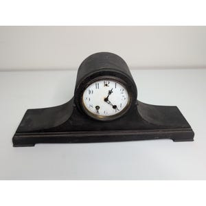May include: A black mantel clock with a white clock face and black hands. The clock has a rectangular base and a rounded top. The clock face features black Roman numerals and a small seconds dial.