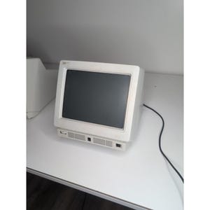 May include: A vintage off-white IBM computer monitor with a black screen. The monitor has a rectangular shape with a vent at the bottom and a black power cable. The monitor is on a white surface.