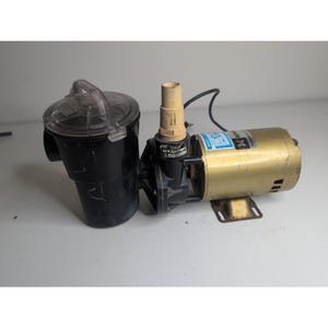 May include: A pool pump with a black filter housing and a clear lid. The pump motor is gold-colored with a black base. A beige pipe extends from the pump. A black power cord is attached.