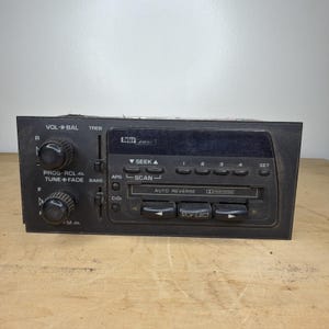 May include: A black Delco Bose car radio cassette player featuring two large circular knobs for volume, balance, tuning, and fade. The front panel includes a cassette slot, buttons for seek, scan, and station presets, and vertical sliders for treble and bass.