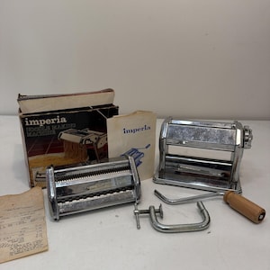 May include: A chrome Imperia noodle making machine set including two metal pasta roller attachments, a hand crank with a wooden handle, a metal C-clamp, an instruction manual, and the original cardboard box with product imagery and text.