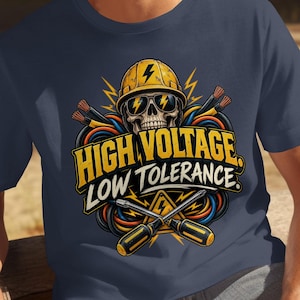 May include: A navy blue t-shirt featuring a graphic of a skull wearing a yellow hard hat and sunglasses, surrounded by colorful electrical wires and two crossed screwdrivers. The text reads HIGH VOLTAGE LOW TOLERANCE.