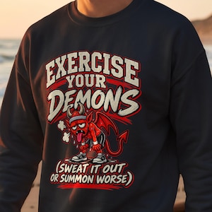 May include: A dark navy blue crewneck sweatshirt featuring a graphic of a red cartoon demon wearing a headband and athletic shorts. The text reads EXERCISE YOUR DEMONS and SWEAT IT OUT OR SUMMON WORSE in bold white and red lettering.