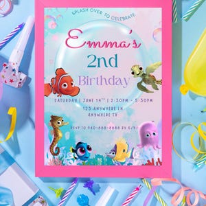 Puede incluir: Una invitación enmarcada en rosa para el segundo cumpleaños de Emma, con criaturas marinas de dibujos animados. La invitación incluye la fecha, la hora y el lugar, con el texto "SPLASH OVER TO CELEBRATE". Los recuerdos de la fiesta y las decoraciones rodean la invitación sobre una superficie azul.