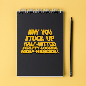 Könnte beinhalten: Schwarzes Spiralnotizbuch mit dem Text "WHY YOU STUCK UP HALF-WITTED SCUFFY-LOOKING NERF-HERDER!" in Gelb. Ein schwarzer Bleistift liegt neben dem Notizbuch auf gelbem Hintergrund. Das Notizbuch ist ein Schreibwarenartikel.