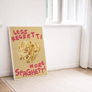 Könnte beinhalten: Ein gerahmtes Poster mit dem Text "LESS REGRETTI MORE SPAGHETTI" in rosa Schrift. Das Bild zeigt einen Teller Spaghetti mit Käse. Das Poster lehnt an einer weißen Wand in der Nähe eines Fensters.