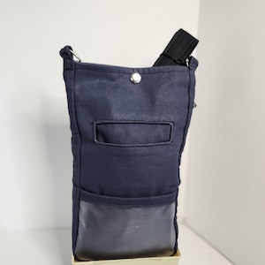 May include: A dark blue canvas crossbody bag with a black strap and a silver button closure. The bag has a small pocket on the front and a clear plastic window on the bottom.