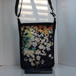 May include: A black crossbody bag with a floral print. The print features white, yellow, orange, and blue flowers on a dark blue background.