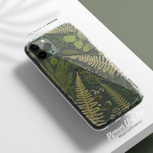 Pode incluir: Uma capa transparente para telefone com um padrão de folhas verdes. A capa tem uma saliência de câmera elevada e o texto "Premium Clear Case" e "@SugarLoafGraphics" impresso na parte inferior.