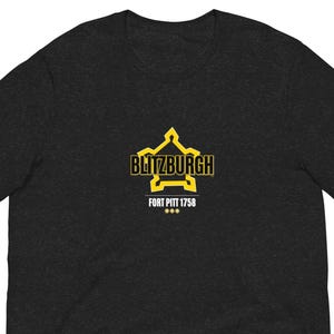 May include: Dark gray t-shirt with a yellow and black graphic that reads "Blitzburgh" above "Fort Pitt 1758". The graphic is a stylized star and building design.