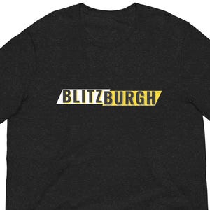 May include: Dark gray t-shirt with the word "BLITZBURGH" in white and yellow block letters. The shirt is short-sleeved and has a crew neck.