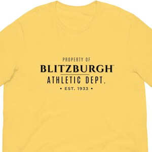 May include: A yellow t-shirt featuring the black text "PROPERTY OF BLITZBURGH ATHLETIC DEPT. EST. 1933". The shirt has a crew neck and short sleeves.