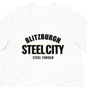 May include: White t-shirt featuring the text "BLITZBURGH STEEL CITY STEEL FORGED" in black and gold lettering. The shirt has short sleeves and a crew neck.