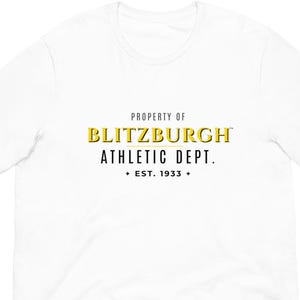 May include: White t-shirt with the text "PROPERTY OF BLITZBURGH ATHLETIC DEPT. EST. 1933" in yellow and black. The shirt has a crew neck and short sleeves. The text is centered on the front of the shirt.