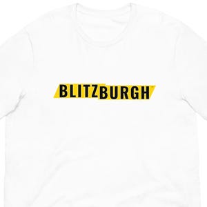 May include: White t-shirt with the word "BLITZBURGH" in black text on a yellow horizontal rectangle. The t-shirt is made of a soft material and has short sleeves and a crew neck.